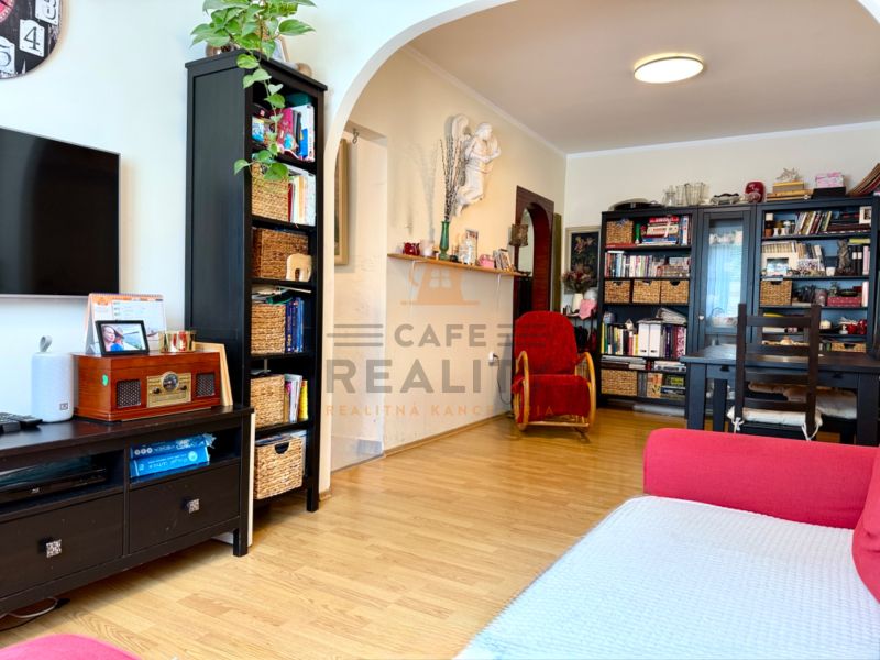 Living room with wood-patterned flooring, black furniture, and a bookshelf in a three-room apartment.