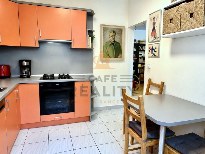 A kitchen in a 3-room apartment with orange cabinets, a dining set placed, and decorations on the walls.