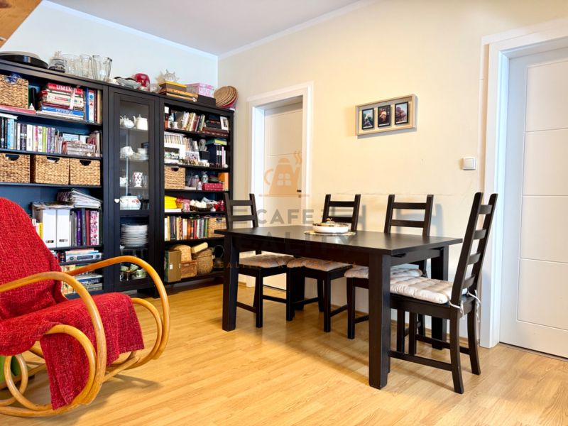 Dining table with chairs, rocking chair, bookshelf, floor with wooden decor.