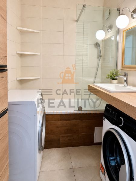Bathroom with a bathtub, washing machines, and a sink in a 3-room apartment, tiles and wooden decor.