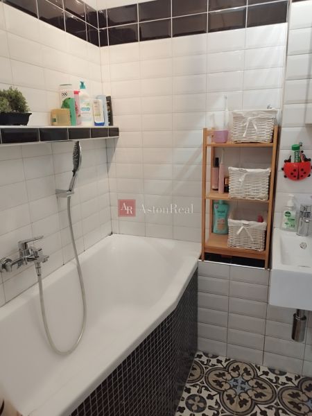 A bathroom in a 2-room apartment with a bathtub, mosaic tiles, and a shelving cabinet.
