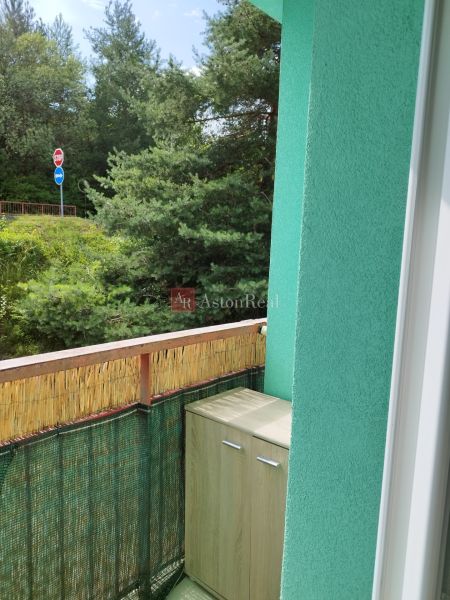The balcony of a 2-room apartment in Banská Bystrica with a view of trees and a road sign.