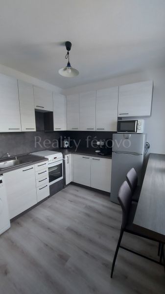 A kitchen in a 2-room apartment with a wood-patterned floor and white cabinets.