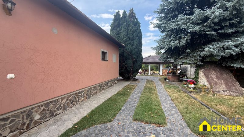 A family house in Iža with a stone exterior cladding, trees, and a landscaped garden.