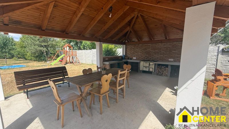 A gazebo at a family house in Iža with wooden furniture and a children's playground in the garden.