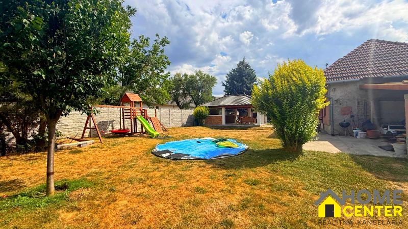 The garden of a family house in Iža with a playground, lawn, and small structures.