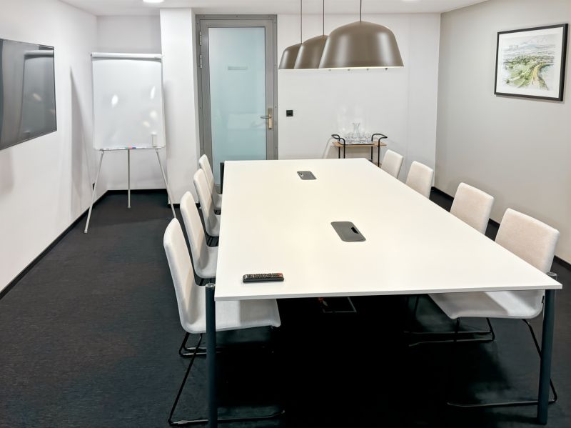 Conference room with a long table, chairs, flipchart, and modern lighting.