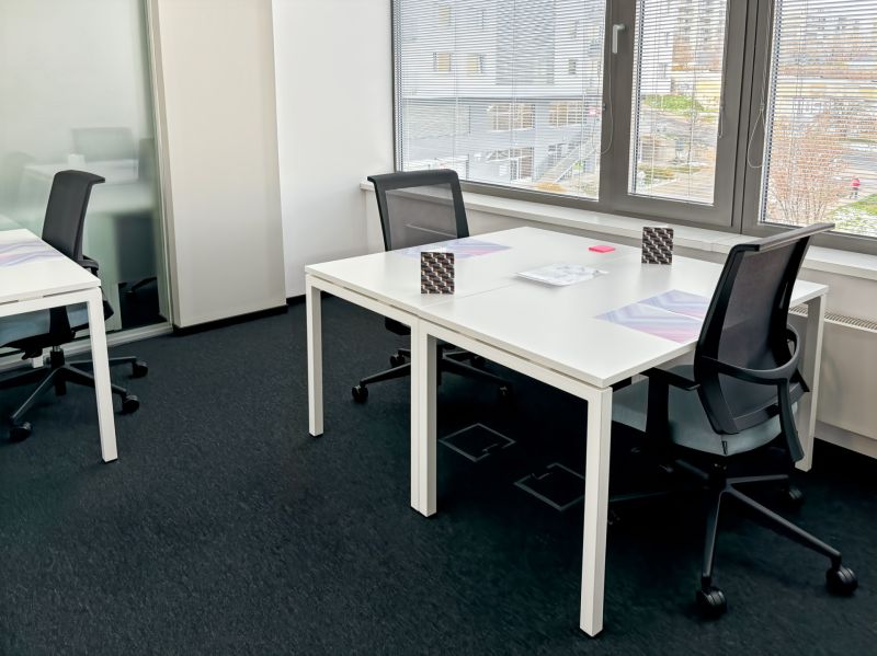 Offices with white desks and black chairs, view from windows with blinds.