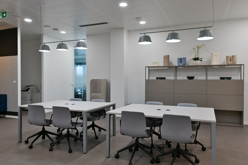 Offices with light gray desks and chairs, pendant lights, shelves with decorations.