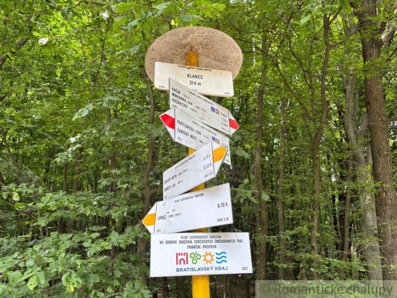 A tourist sign in the forest near a cabin in Bratislava IV, surrounded by dense green vegetation.