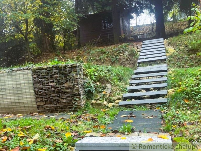A cabin in Bratislava IV surrounded by a green slope and a staircase made of gray planks.
