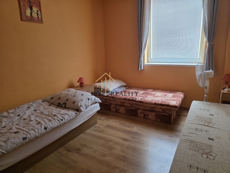 A room with two beds, a wooden decor floor, orange walls, curtains, a window.