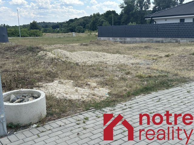 A plot for residential use in Lučenec with a grassy area and a paved walkway on the edge.