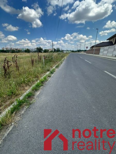 A path near residential plots in Lučenec with a field in the background.