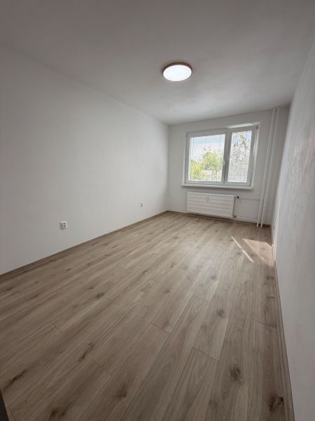 A room with a wooden decor floor in a 2-room apartment, white walls, and a window.