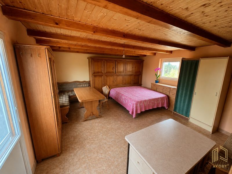 A room in a cottage with a wooden ceiling, a bed, a wardrobe, and a table with chairs.
