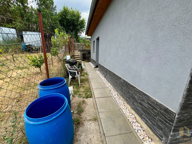 A cottage in Skalica with a side area and blue barrels by the fence.