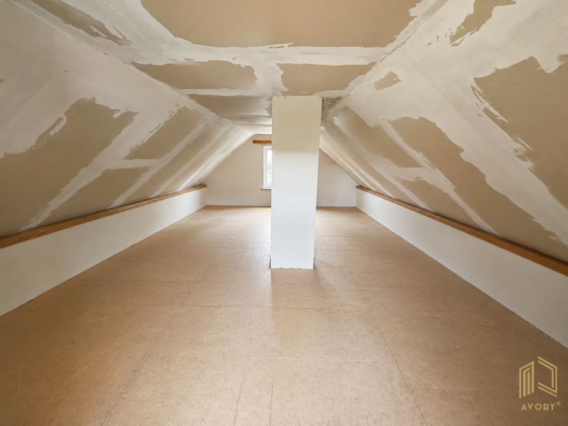 Attic space in a cottage with a wooden decor floor and slanted walls.