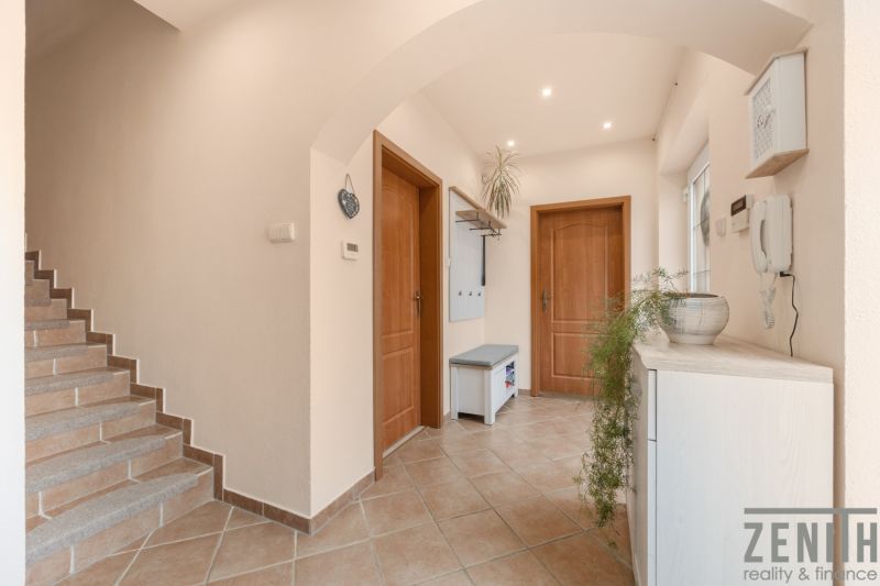 A hallway with tiles and a staircase, entrance to rooms in a family house.