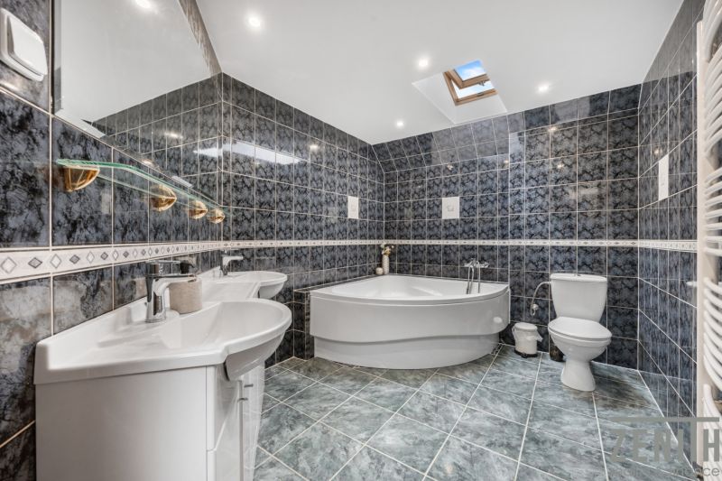 A bathroom in a family house with dark tiles, a bathtub, a toilet, and sinks.