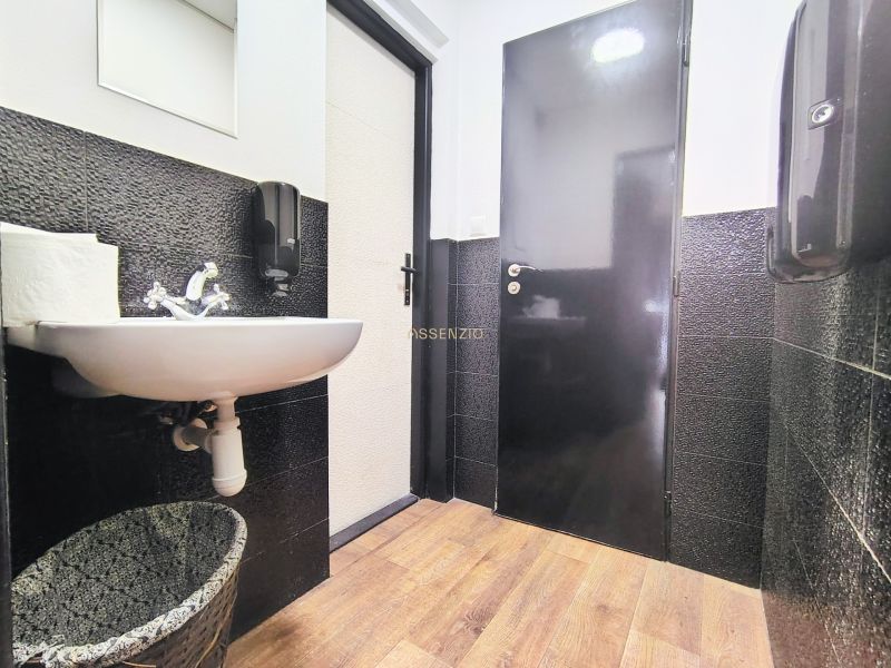 A restroom in a gastro space with black tiles and a floor with a wood design.