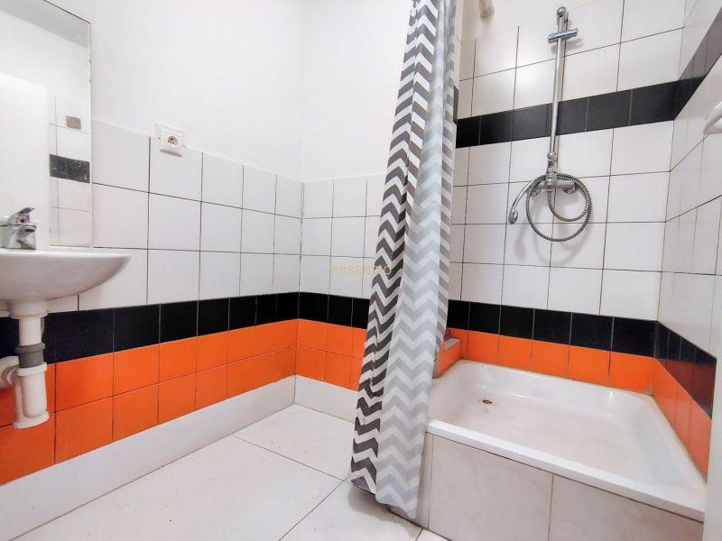 A bathroom with orange and black tiles, a shower corner, and a curtain with a geometric pattern.