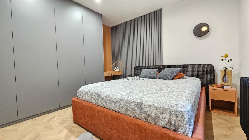 Bedroom with a bed, nightstand, and wardrobe in a 2-room apartment; floor with a wooden decor.