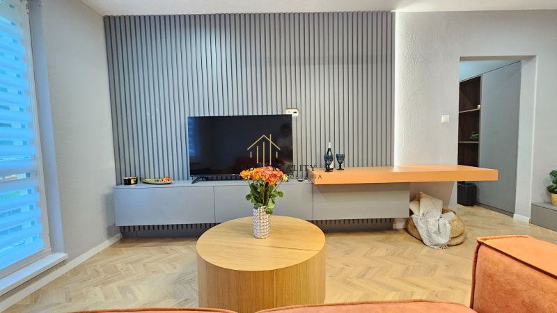 Living room in a 2-room apartment with a television, wooden floor decor, floral decoration.