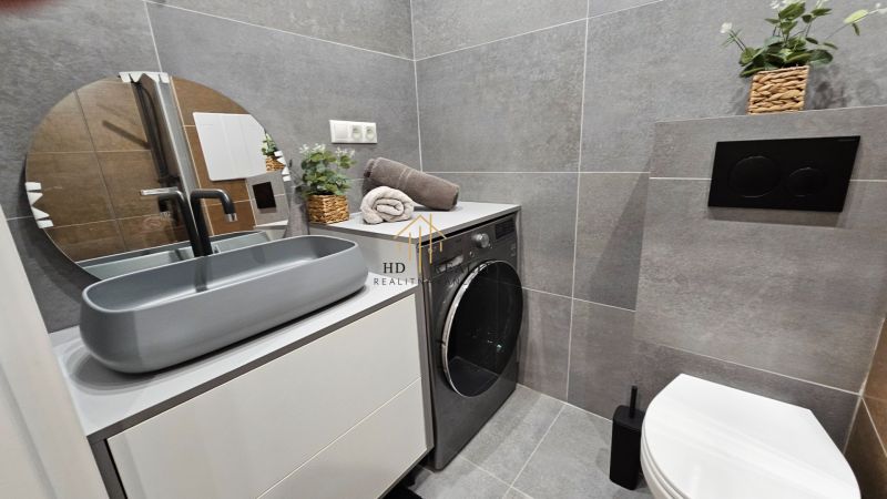 A bathroom with a washing machine and gray tiles in a 2-room apartment.