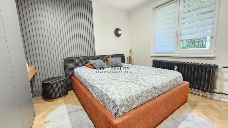 Bedroom in a 2-room apartment with a comfortable bed, a wall with slats, and a floor with a wooden decor.