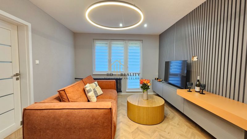 Living room in a two-room apartment with a sofa, a round table, and a wooden decor floor.