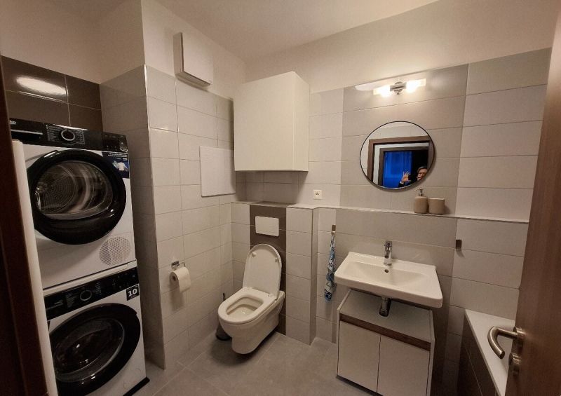 Bathroom in a 2-room apartment with a shower, washing machine, sink, and toilet.