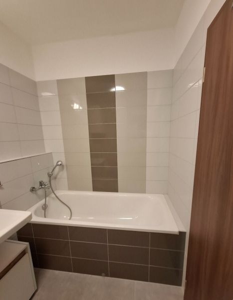 A bathroom with a bathtub and gray tiles in a 2-room apartment.
