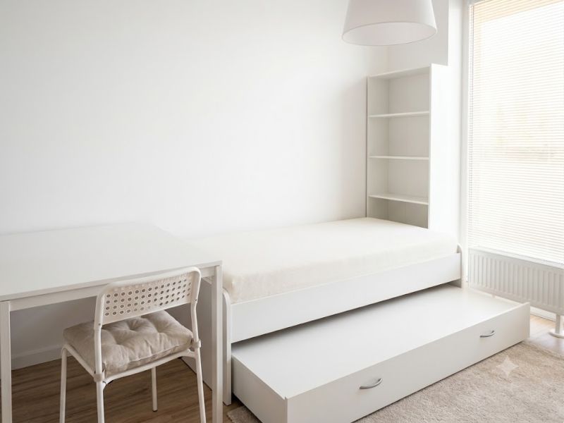Studio apartment with a bed, desk, shelving unit, and floor with wood decor.