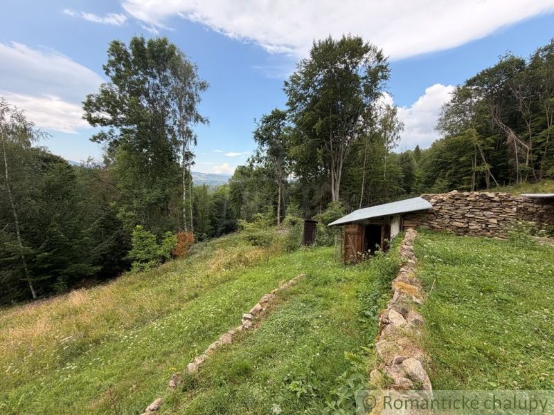 A garden with a stone wall by a family house in Kokava nad Rimavicou, surrounded by forests.
