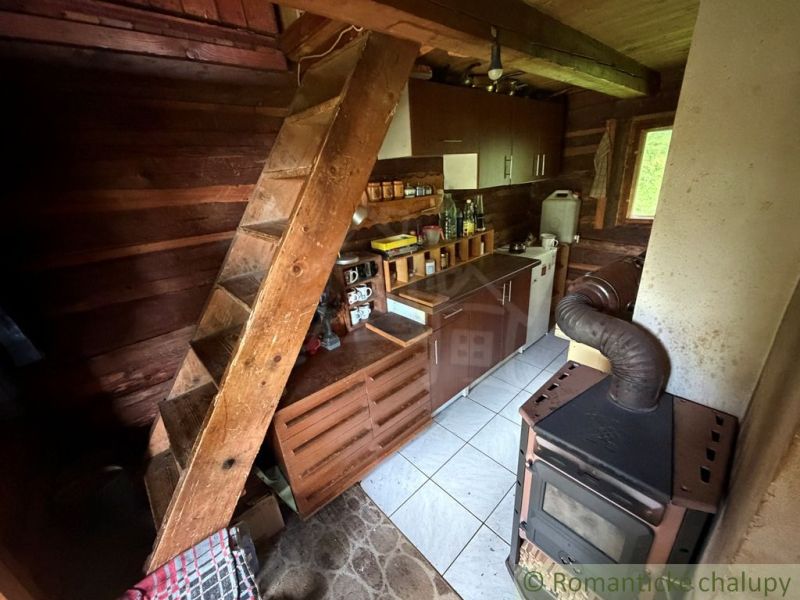 A kitchen in a family house with stairs, wooden walls, and a wood stove.