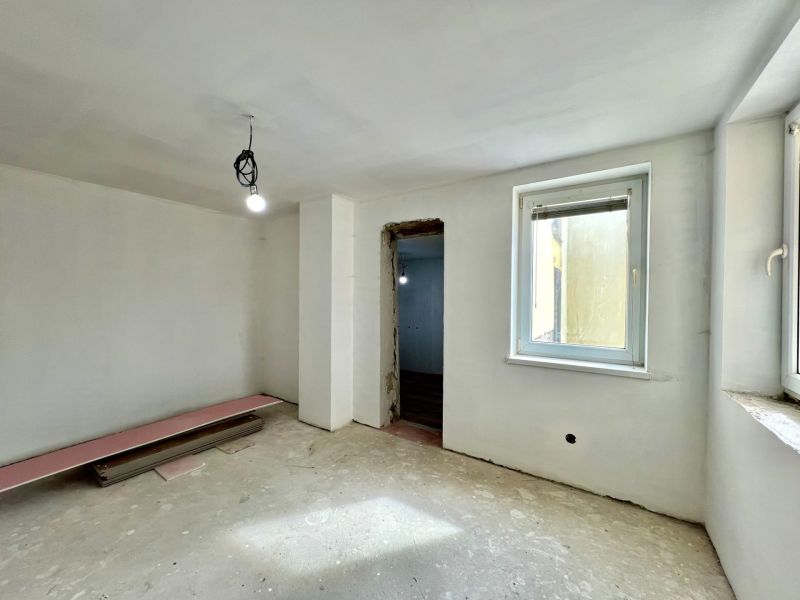A room in a family house with plastered walls and an open window, without flooring.