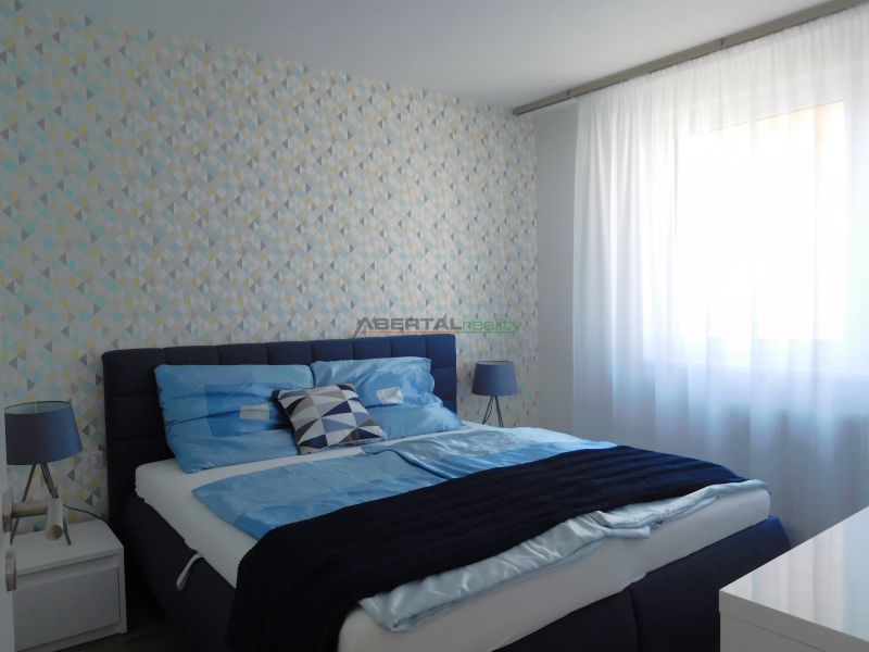 A bedroom in a 2-room apartment with blue bedding and patterned wallpaper.