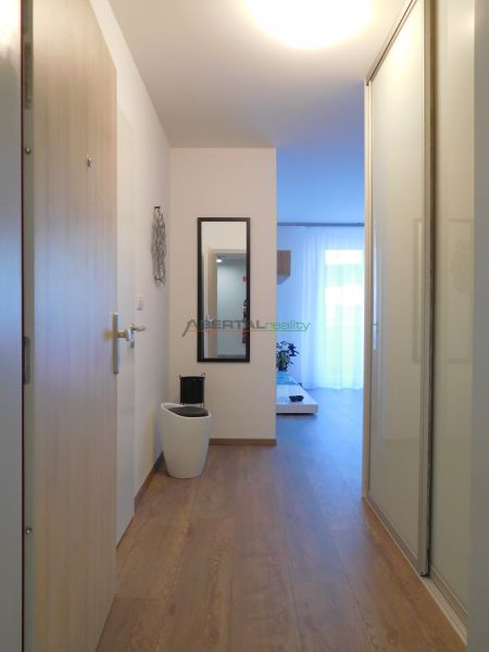 Hallway of a 2-room apartment with a wooden decor floor, mirror, and bright lighting.
