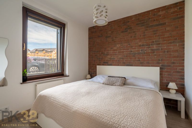 A bedroom in a 2-room apartment with a brick wall and a window with a view.