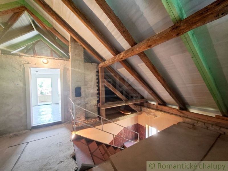 The attic of a family house with exposed wooden beams and a staircase to other areas.