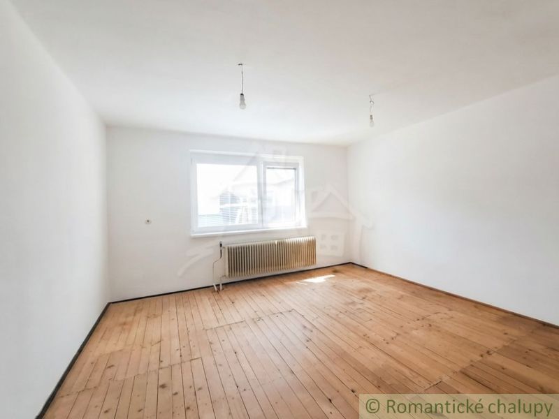 A room in a family house with a wooden decor floor and a window with a radiator.