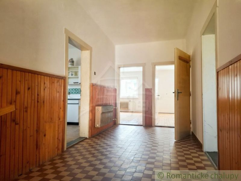 A hallway in a family house with paneling, tiles, and open doors to the rooms.