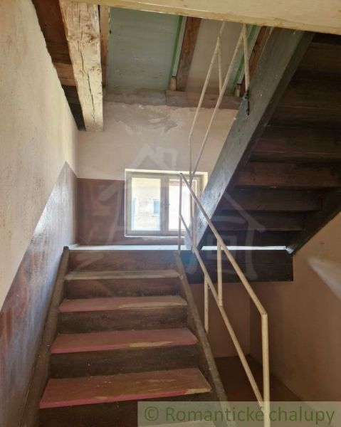 A staircase in a family house, walls with peeling plaster, wooden beams on the ceiling.