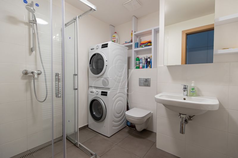 Bathroom with a washing machine and dryer in a studio apartment, light tiles and a shower corner.