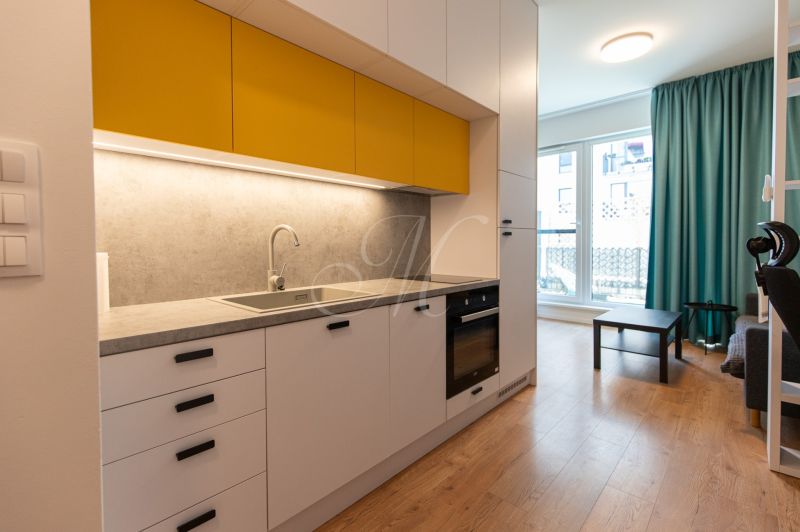 A kitchen in a studio apartment with yellow cabinets and a wooden decor floor.