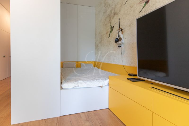 A bedroom in a studio apartment with a bed, TV, and wooden decor flooring.