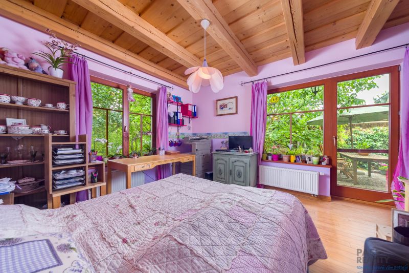 The interior of a family house with a wooden ceiling, purple curtains, and a bed.