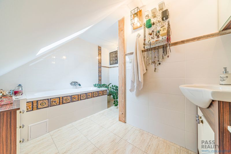 A bathroom in a family house with a bathtub, tiles with ornaments, and a jewelry hanger.