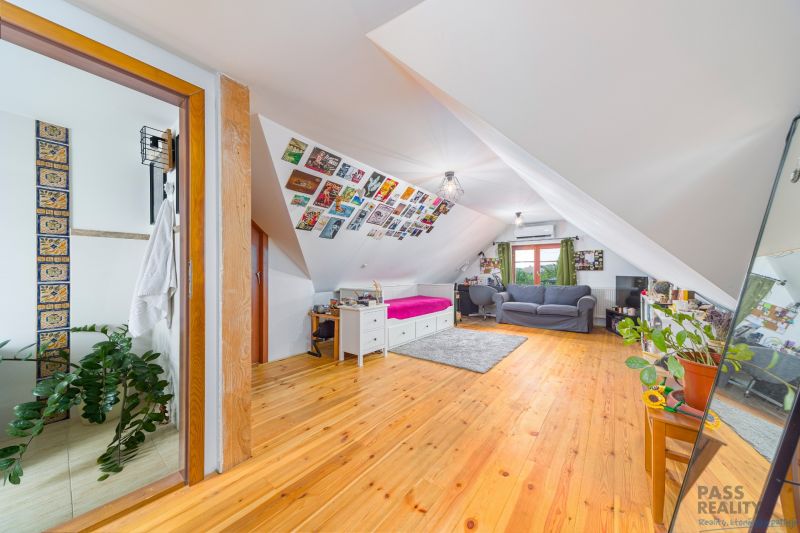 Attic room with a bed, sofa set, and wooden decor flooring in a family house.